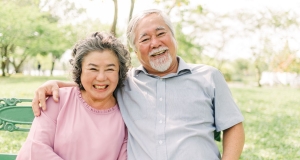 Elderly couple sitting on bench with husband's arm around wife